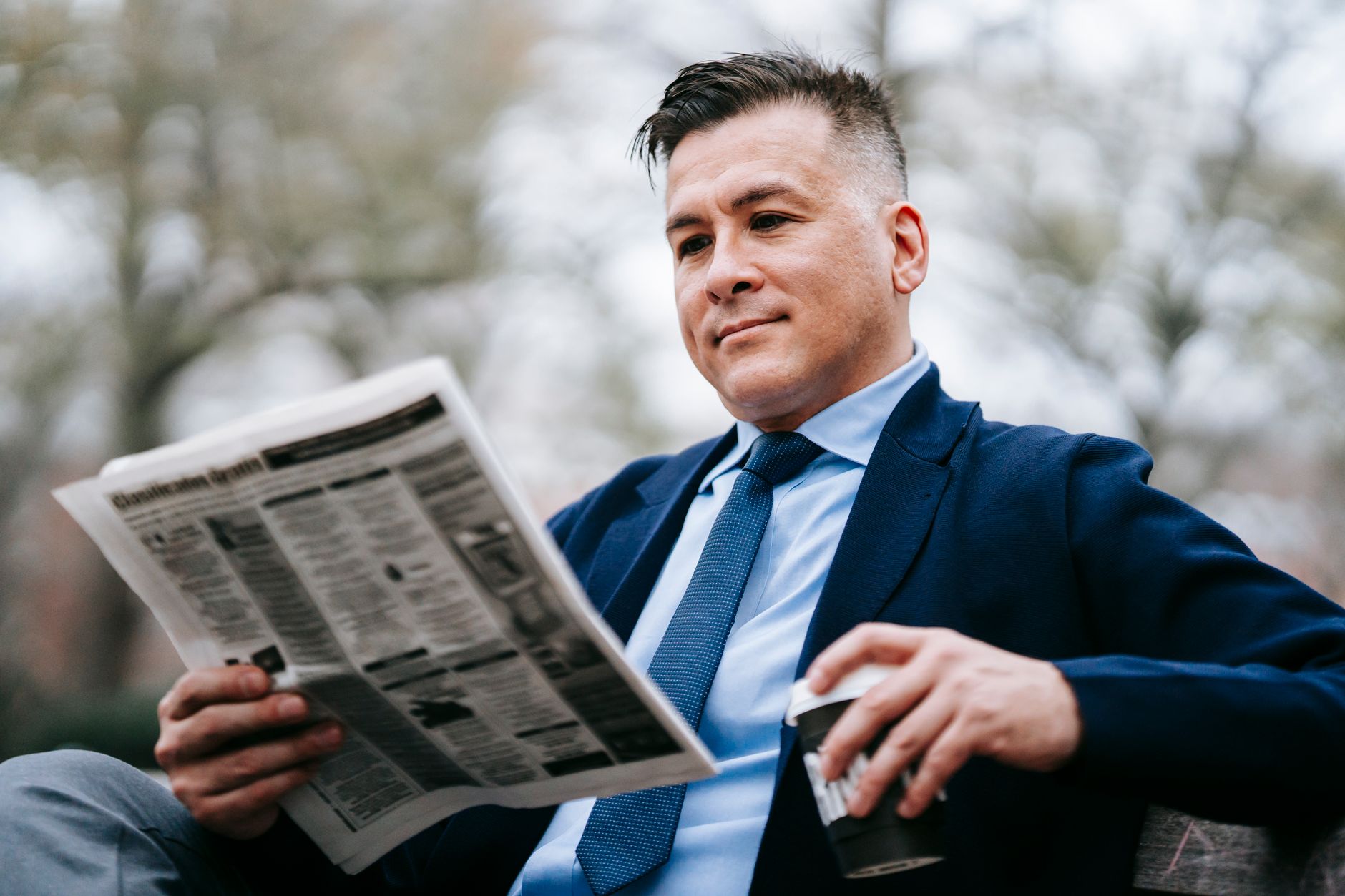 Stylish man in formal wear enjoys a drink while reading a newspaper outside. — test123123